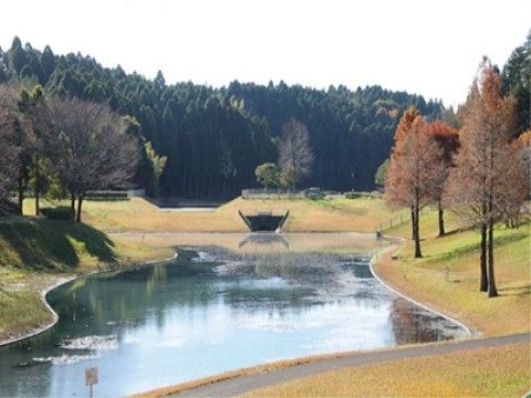 公園には大きな池があり、周りは芝生で囲まれている。池の周囲には木々が立ち並び、遠景には緑の山が見える。