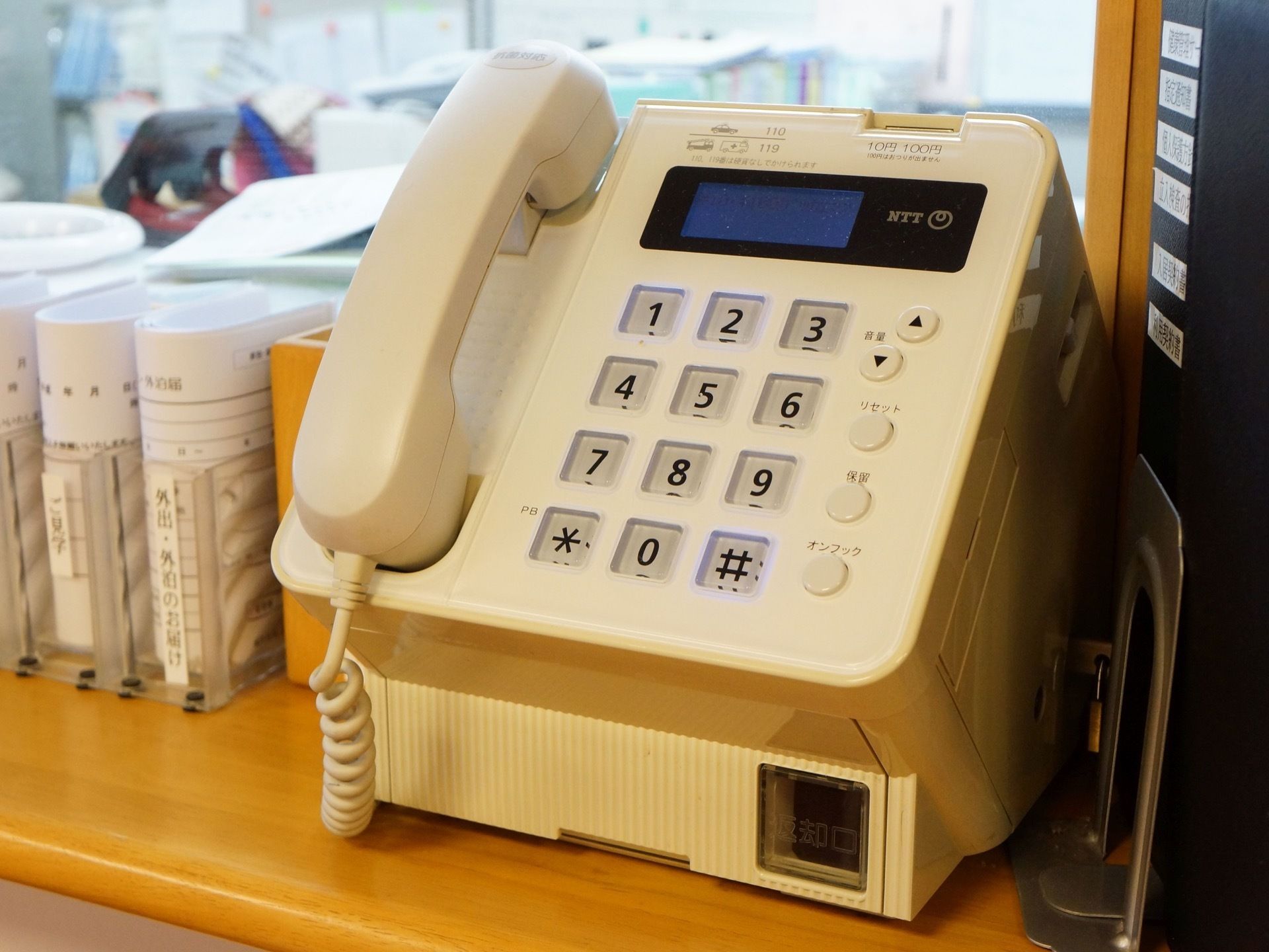 スタッフルーム前のカウンターには白い公衆電話が設置されている。外出、外泊時の届け出用紙が置かれている。