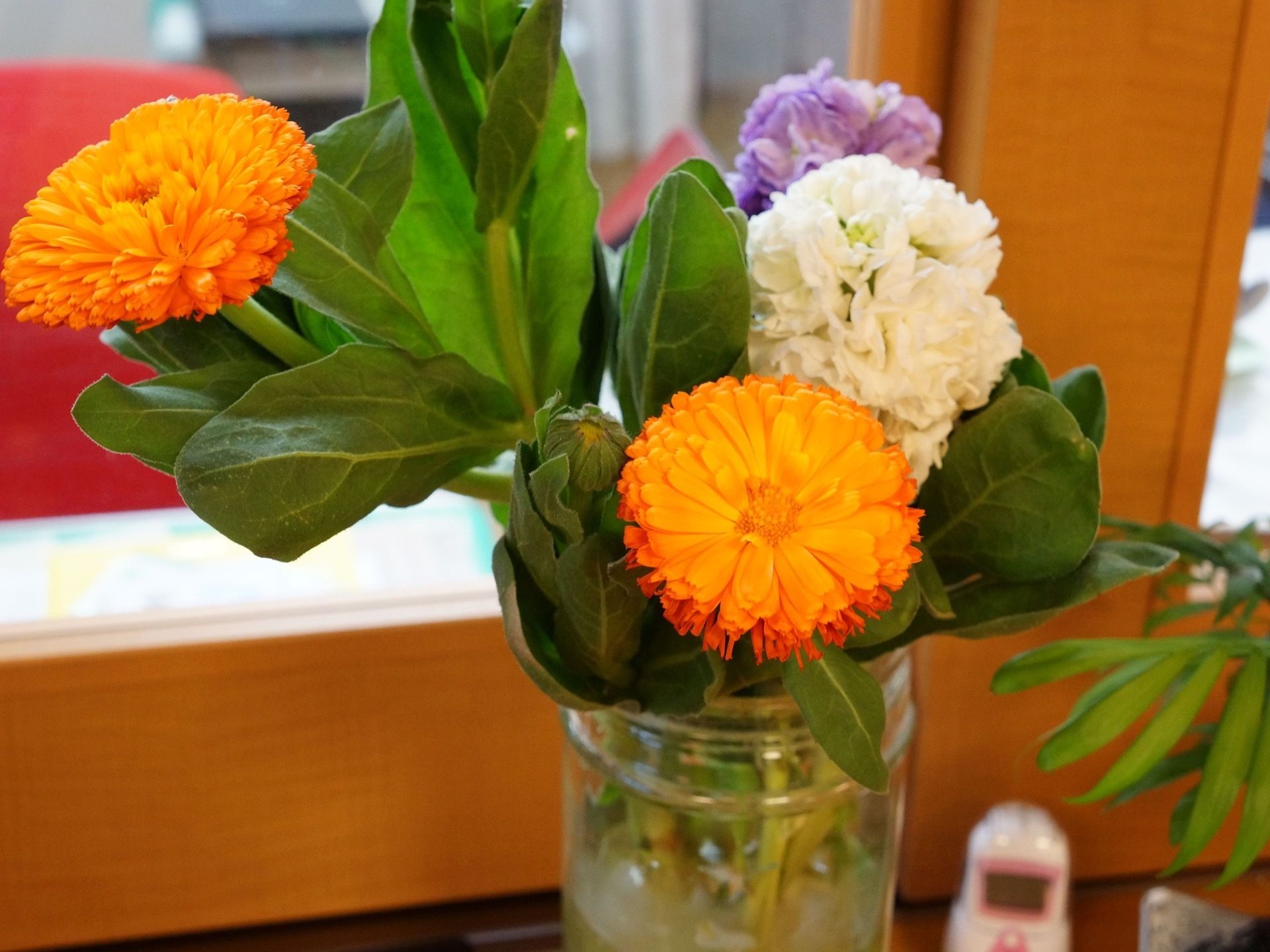 透明の瓶に花が生けられ、スタッフルームのカウンターに置かれている。オレンジ、白、紫の花が咲き誇っている。