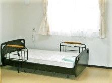 介護用ベッドが壁際に置かれたフローリングの居室。日当たりがよく、窓にはカーテンも付いている。