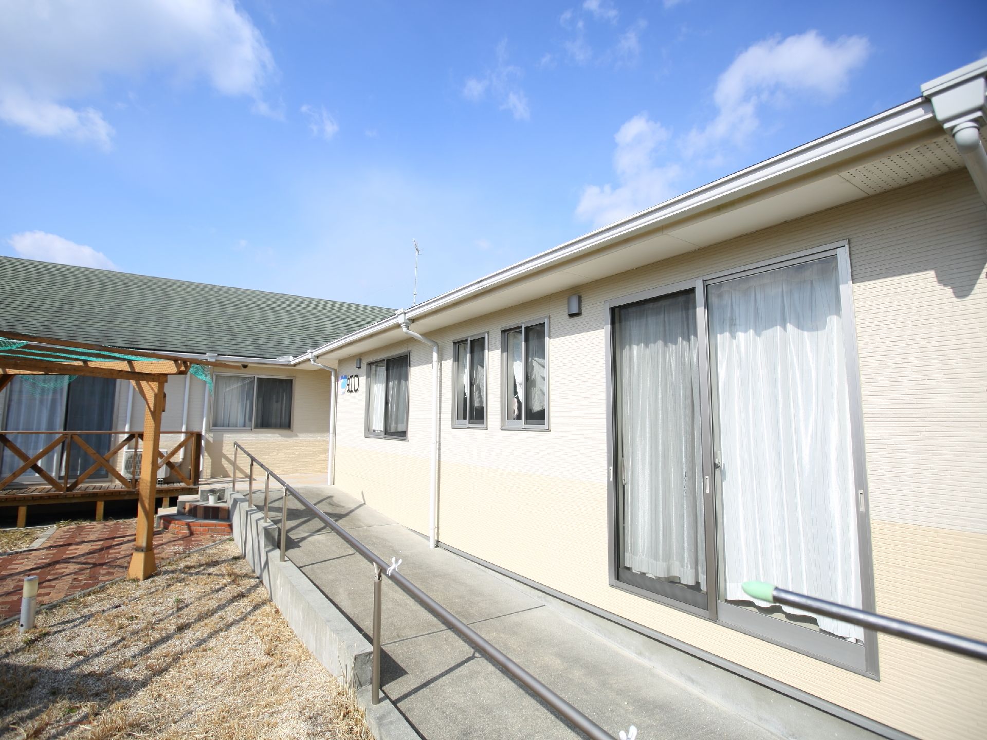 クリーム色を基調とし、手すり付きスロープが設置されている平屋の外観