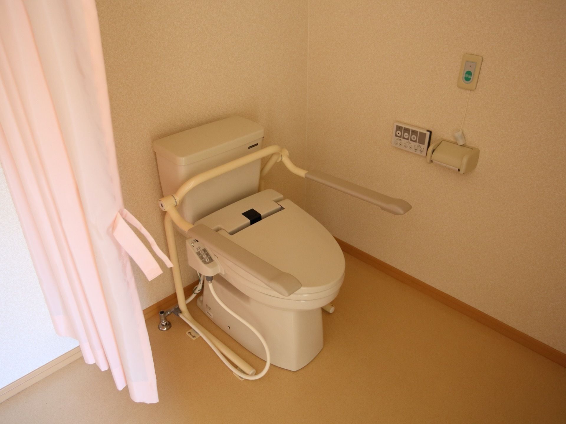 居室に備えているトイレである。扉ではなく、カーテンが使われている。立ち座りを補助する手すり両側にある。