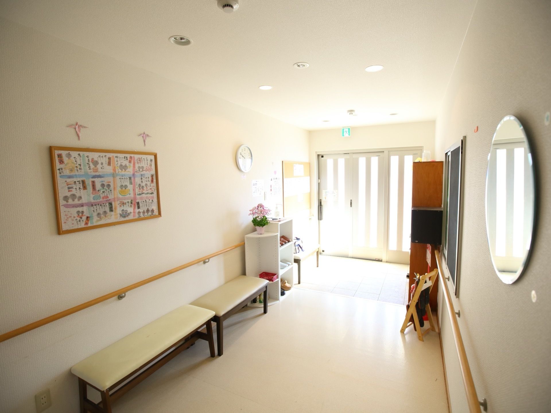 光が多く入り込んでいる玄関である。ベンチがいくつも並べられており、その横にはスリッパが置かれている。