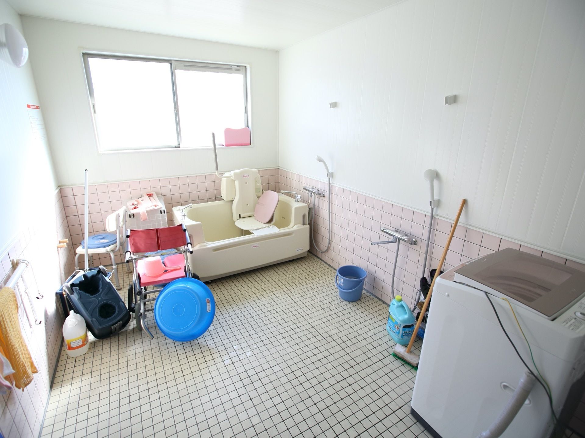 窓がある広い浴室である。機械式浴槽や洗濯機が設置されている。シャワーチェアーや車椅子がある。