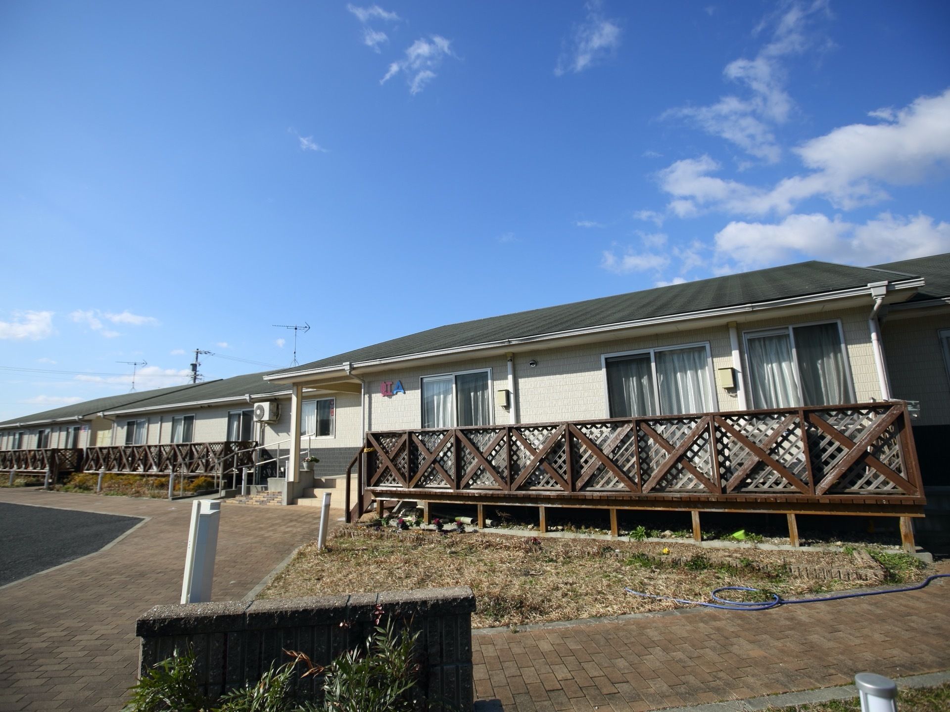ホテルのような可愛らしい外観である。平屋でそれぞれの居室の外にはウッドデッキが備わっており、窓にはカーテンが下がっている。