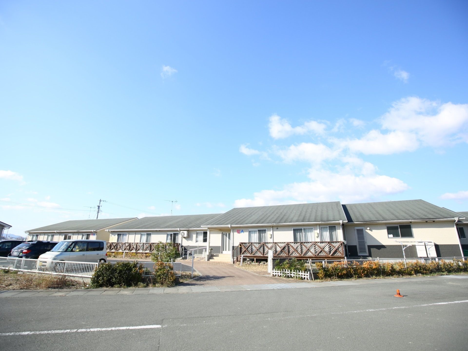 コテージのような外観である。緑色の屋根の平屋であり、居室から出られるウッドデッキがある。日差しが多く降り注いでいる。