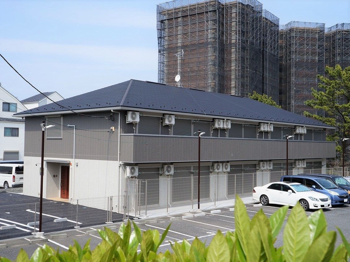 手前に駐車場スペースがある施設の外観。グレーと白のツートンカラーの建物