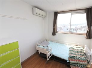 大きな窓があり明るい雰囲気。居室には、ベッドや収納家具だけでなくエアコンもついている。