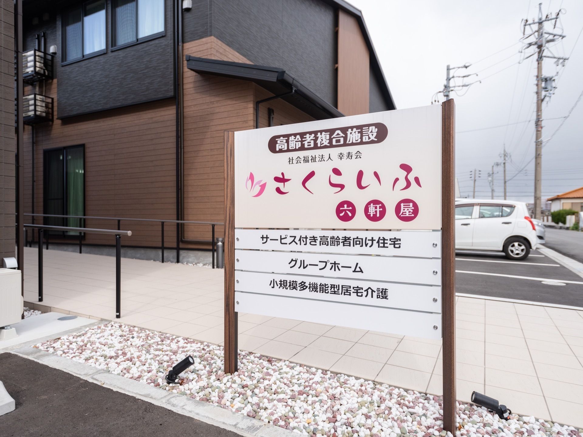 茶と黒をベースとした、シックな雰囲気の施設の外観。車道の近くの目立つ場所に、案内看板が立てられている。