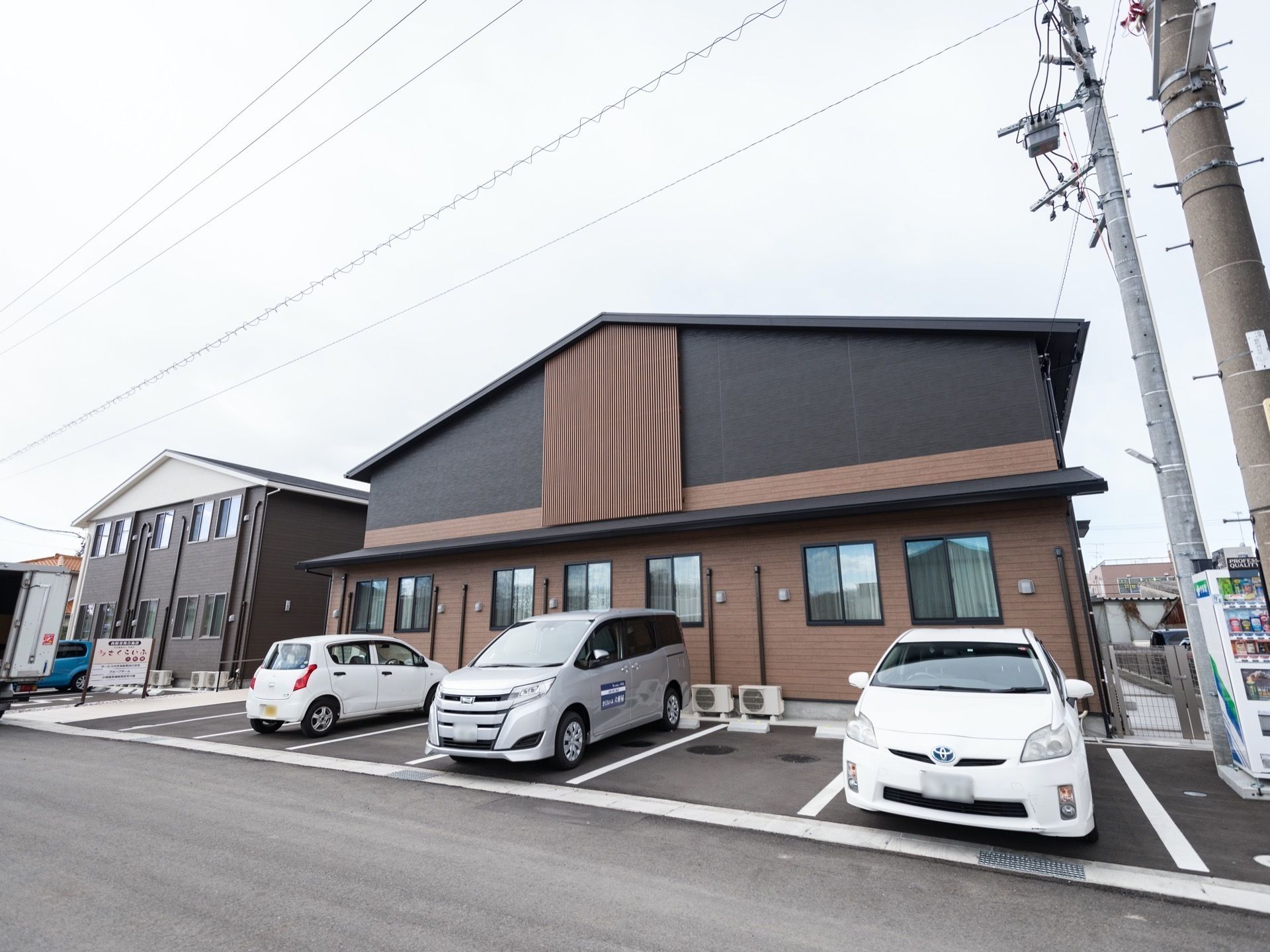 駐車場が付いた2階建ての建物。黒とベージュで和の雰囲気が漂い、三角の屋根が付いている。