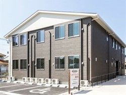 グレーの建物は２階建て手駐車場があり、駐車場の前には看板も設置されている。