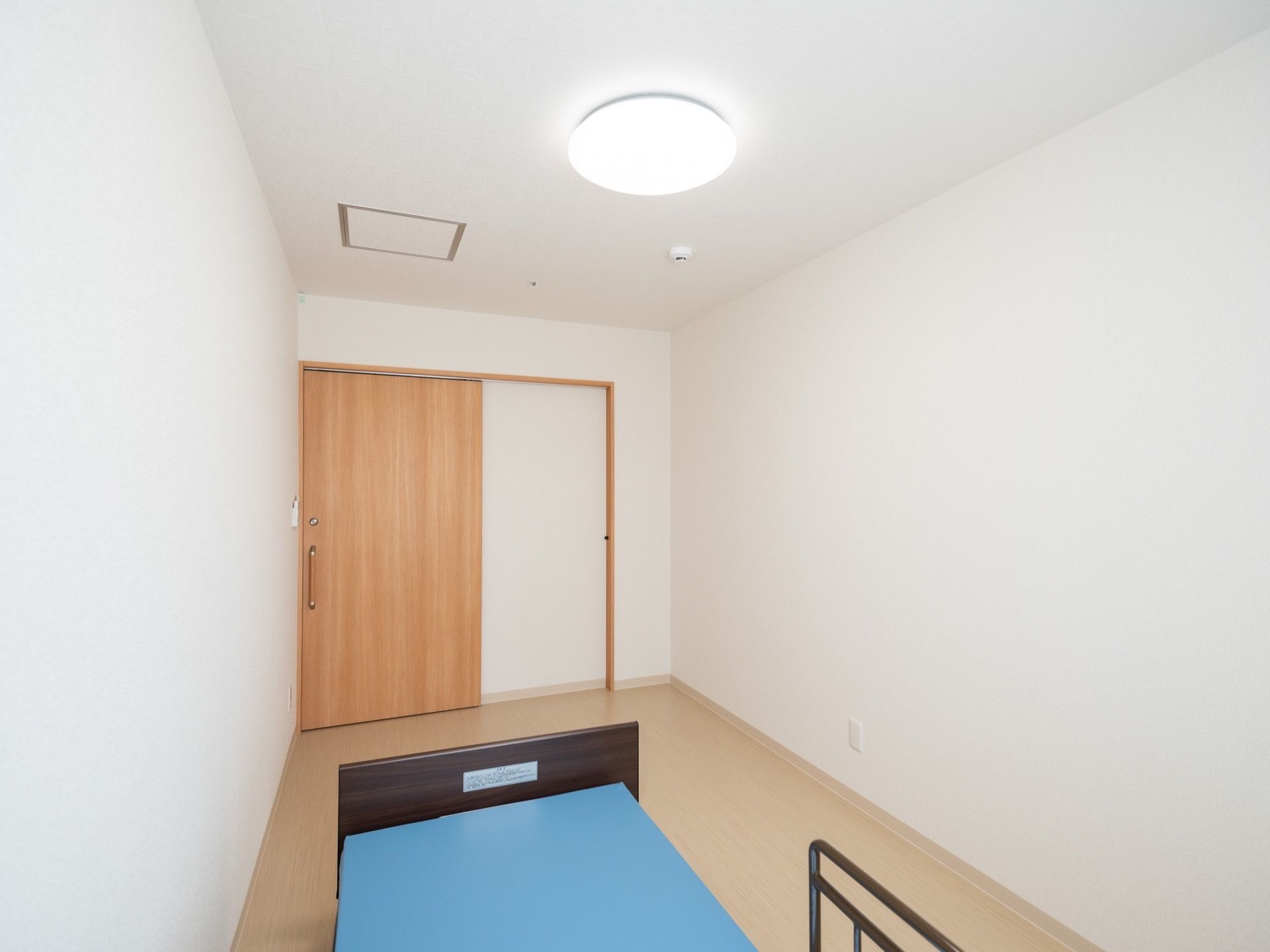 居室の扉は木製のスライドドアである。天井にはシーリングライトのほか、火災報知器とスプリンクラーが設置されている。