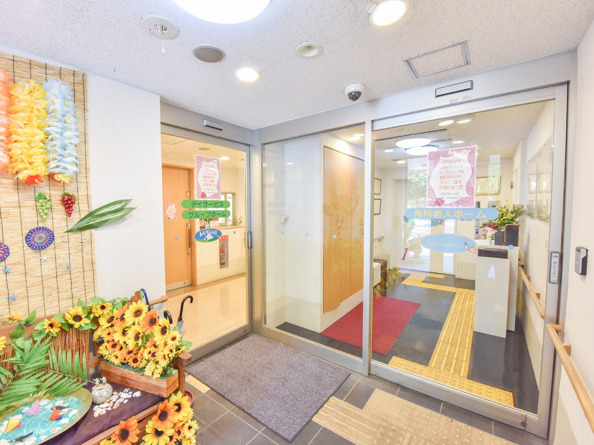 2つの自動ドアがあるホールには夏らしい装飾がある。正面のドアに「有料老人ホーム」、左手ドアに「デイサービス」「グループホーム」と書いてある。