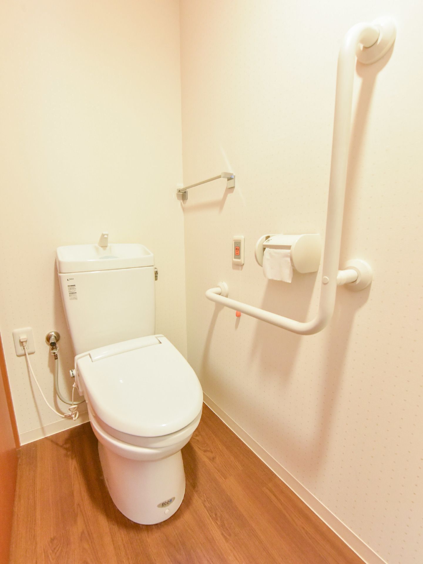 居室のトイレには、左手の壁にL字型の手すりとタオル掛け、トイレットペーパーのホルダー、呼び出しボタンが付いている。