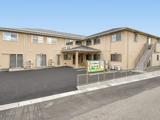 エル字型の2階建ての建物が広い駐車場が広い中ある敷地内にあり、屋外階段も付いている。