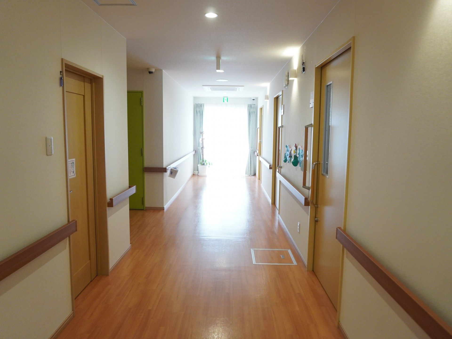 左右にまっすぐな廊下が伸びていて、壁には手すりが設置され、居室のドアも並んでいる。突き当りに窓があり明るい雰囲気。