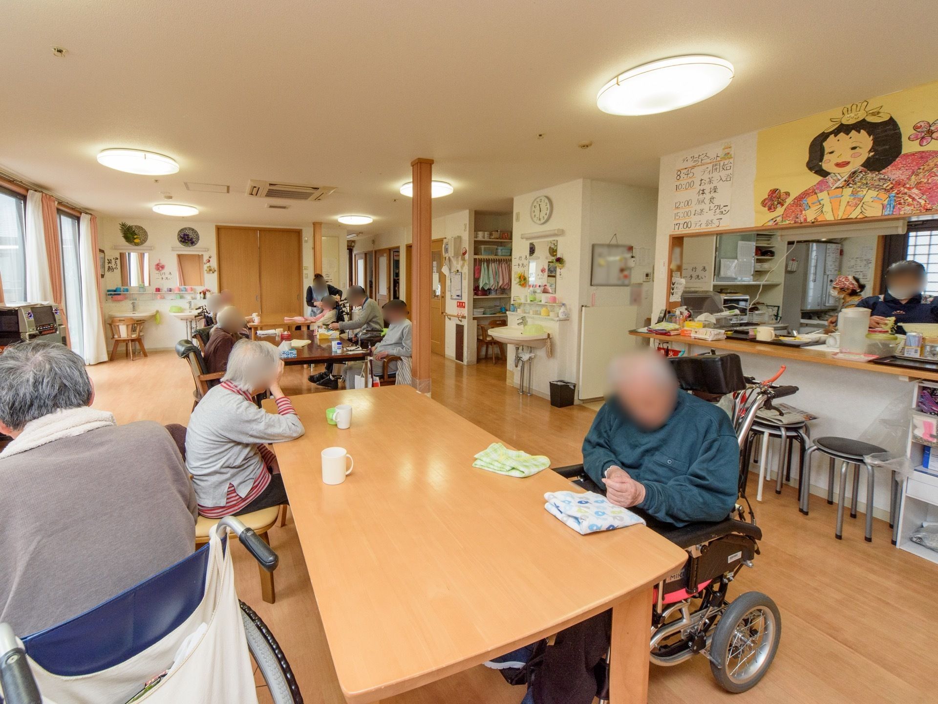 空調や照明の付いた、明るく広いフロアがある。３ヵ所あるダイニングテーブルに入居者が集まって腰を掛けている。