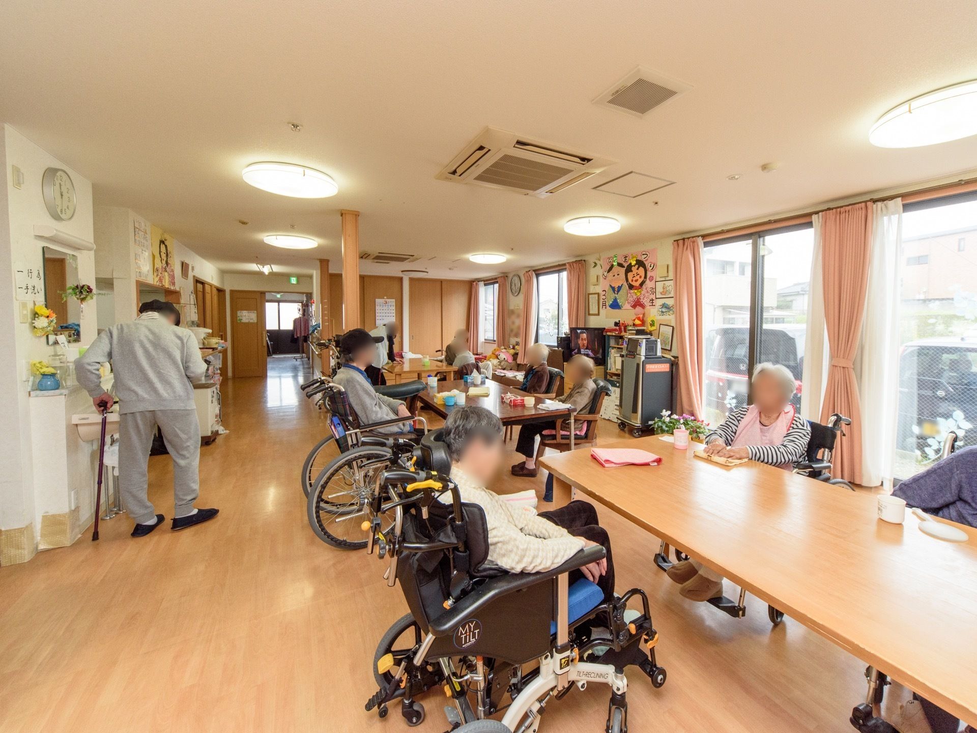 掃き出し窓から外光が入る明るい食堂がある。木目調のテーブルセットが３ヵ所あり、入居者がくつろいでいる。