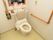 便座に背もたれや手すりが備え付けられたトイレがある。横の壁には、緊急用の呼び出しボタンが設置されている。