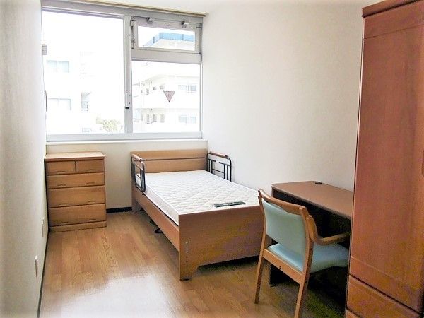 大きな窓が付いたシンプルな居室。寝具付きのベッドやテーブルセット、収納が付いている。