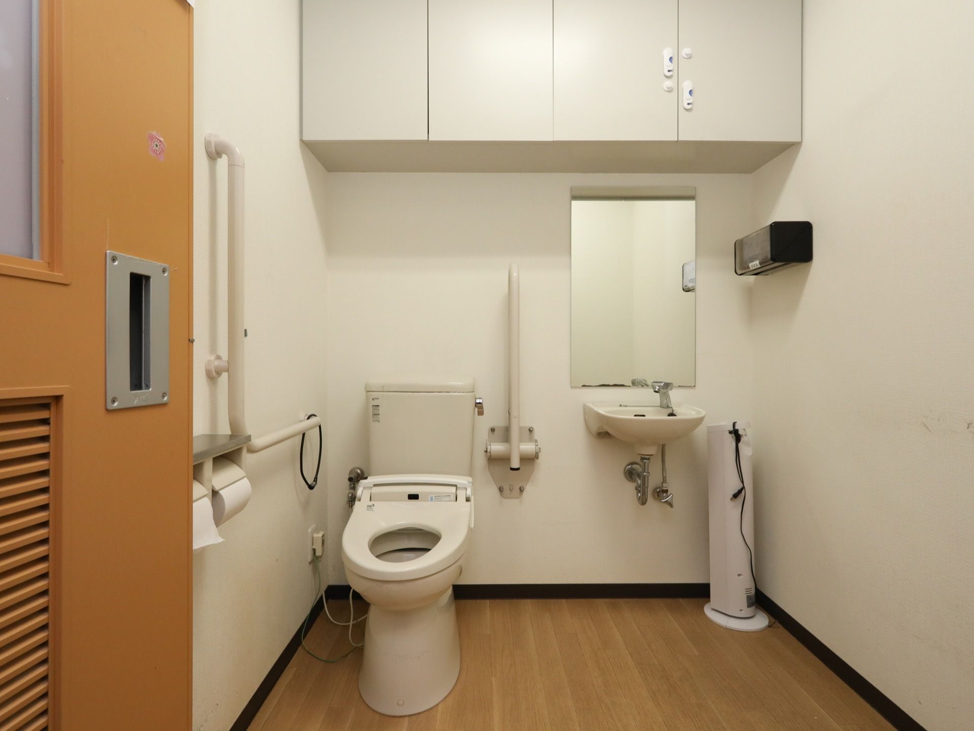 トイレは共有だけですが手すりが完備されている。洗面台も用意されているほか、上部には収納棚が設けられ、備品が収められている。