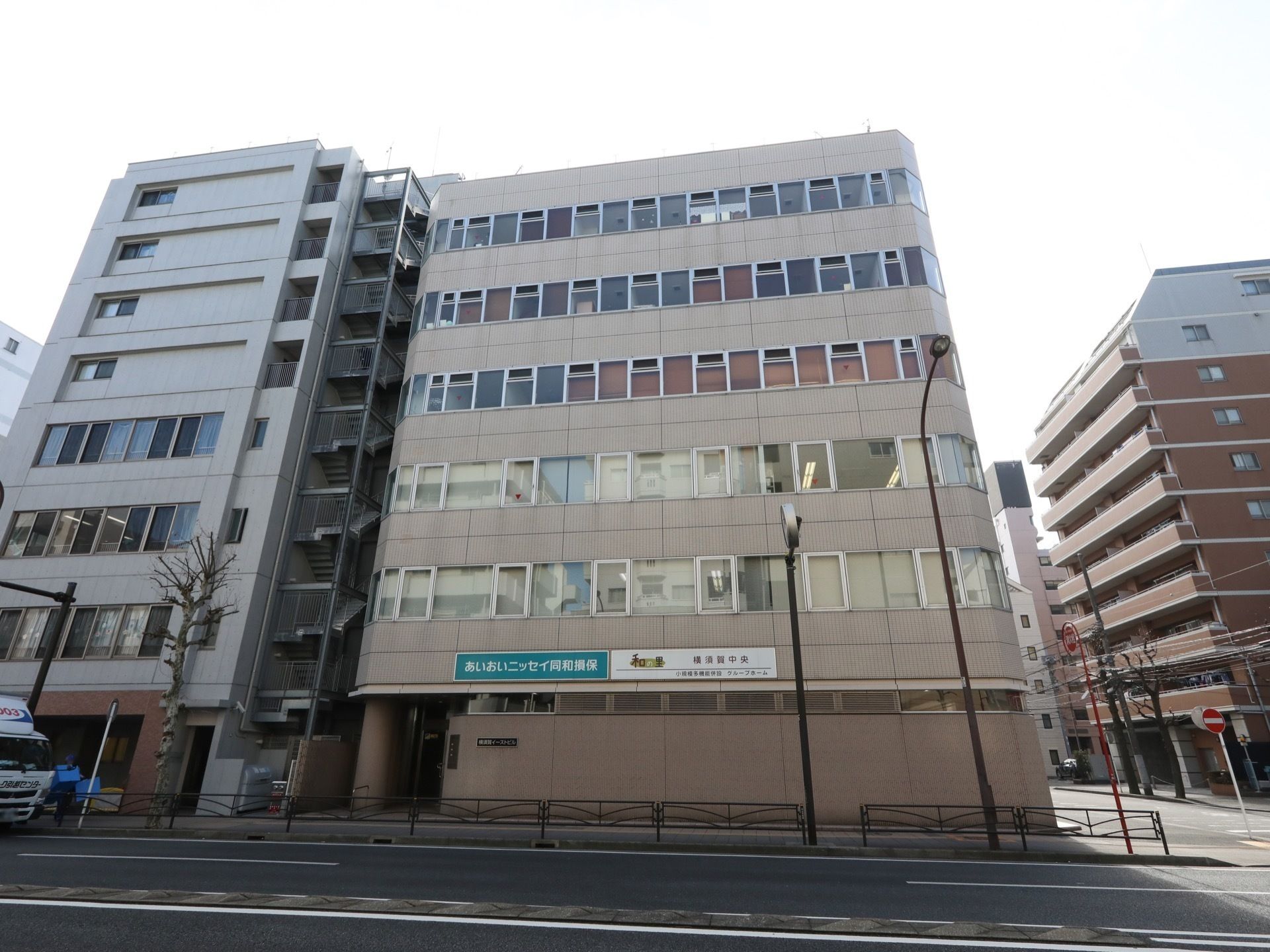 グレーの６階建ての建物には窓がたくさんつき、縦に長く、道路のすぐそばにある。