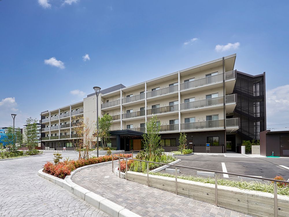5階建ての建物は横に長く、各フロアにベランダがあり、1階部分は白、2階より上の風呂はブラウン系で落ち着いた雰囲気。夕暮れ時で空が一部赤みを帯びている。
