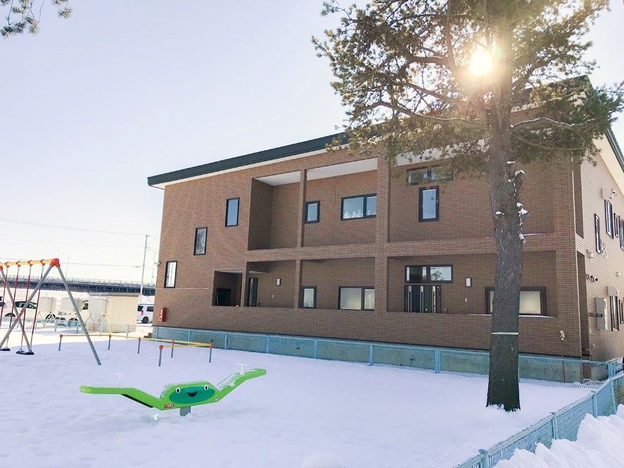 2階建てのブラウンの建物は横に長く窓がたくさんある。目の前には広い公園もある。