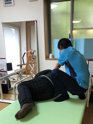 理学療法士によるリハビリを施している様子。ベッドの上に寝ている高齢者と施術している人