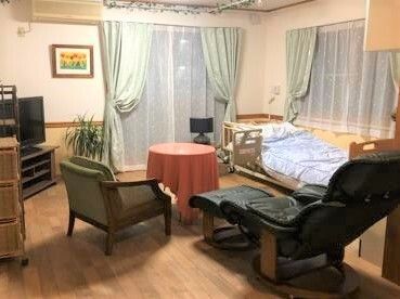 絵画や観葉植物が置かれたフローリングの居室には、寝具付きのベッドやテレビ、テーブルセットやリクライニングチェアもある。