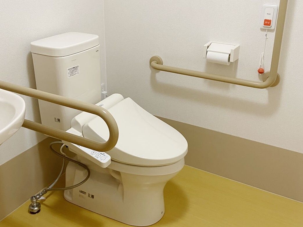 手すりやオレンジの呼び出しボタンが付いた広いトイレ。便座のふたは閉まっている。