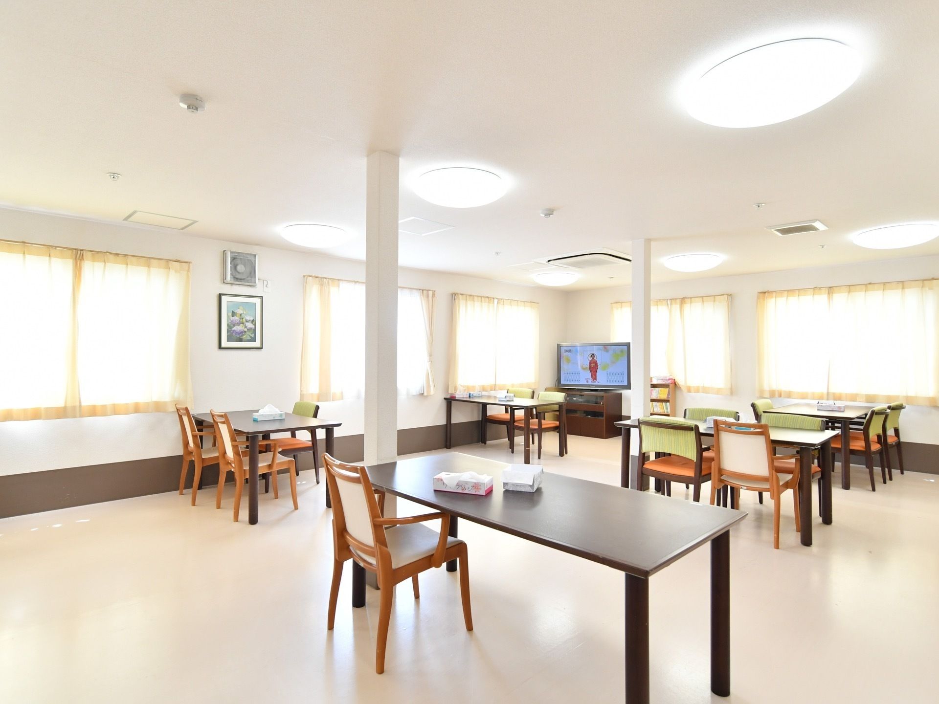 クリームイエローのカーテンがあたたかみのある、広々とした部屋に、ダイニングテーブルや、キッチンチェアが並べられている。