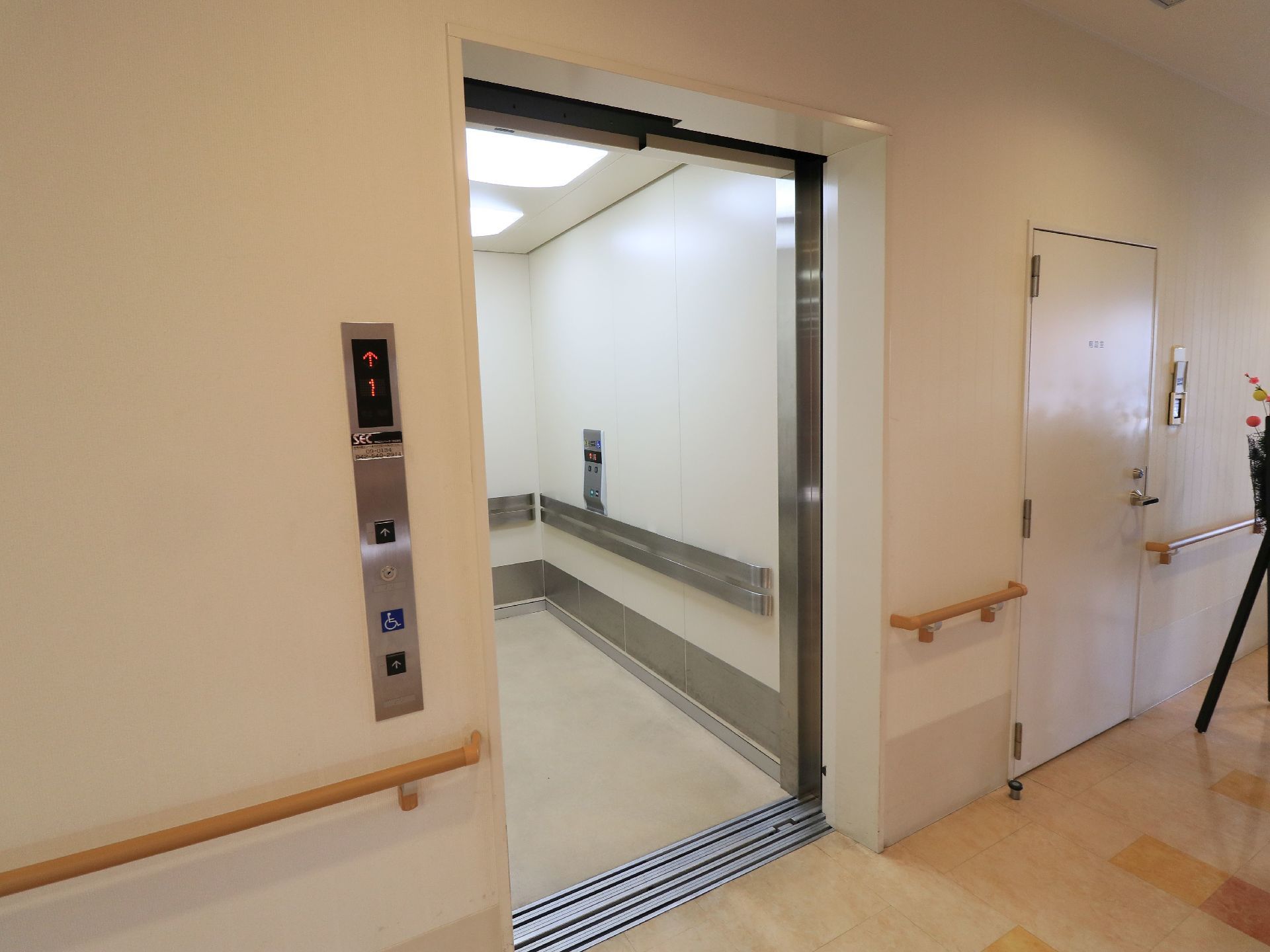 間口の広いエレベーターである。内部や外側の壁には、手すりが設置されている。ひときわ明るい照明が取りつけられている。