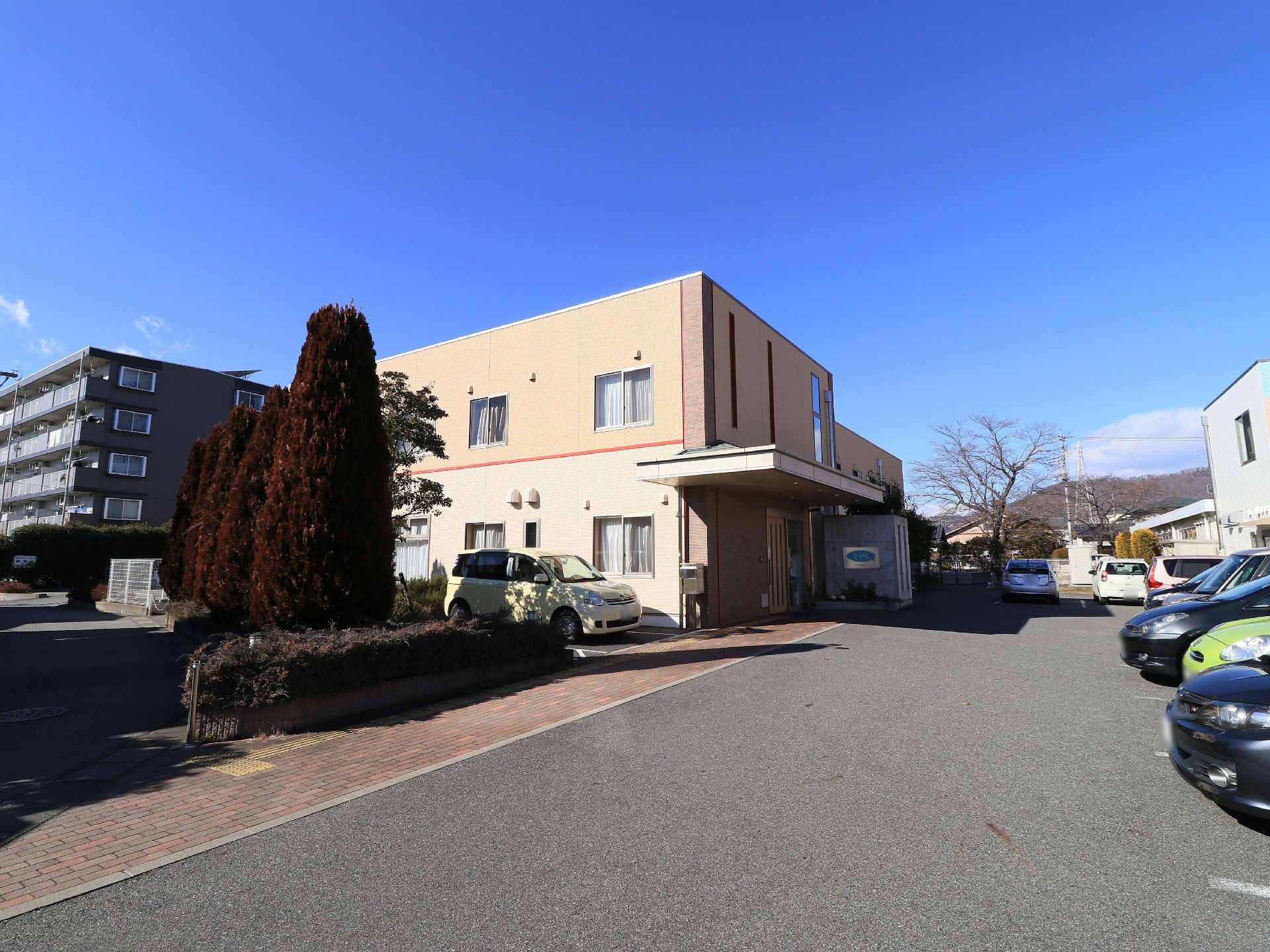 ライトブラウンを基調とした２階建ての施設建物である。通路は、レンガ調の歩道とアスファルトの車道とに分けられている。