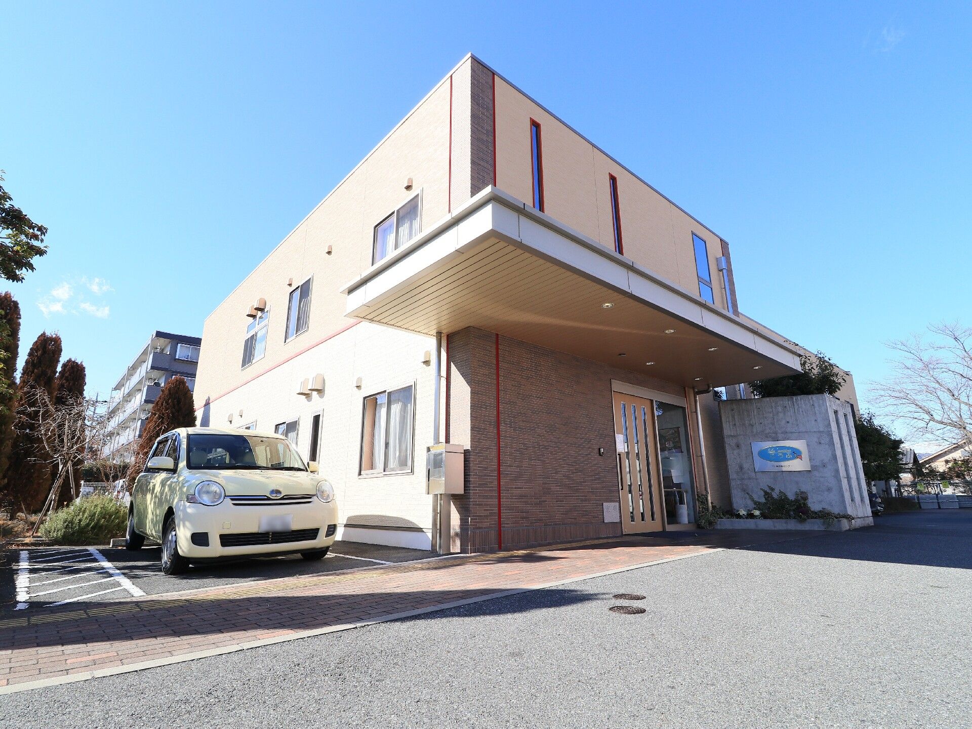 ボックス型の建物で、エントランス部分に平な屋根が張り出している２階建て施設の外観