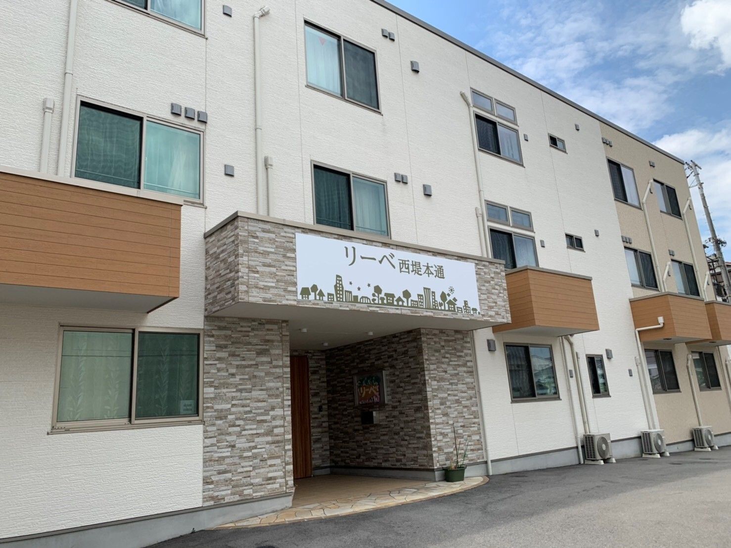 玄関には施設名が書かれた屋根があり、3階建ての建物の玄関に段差はなく、玄関の周りだけ外壁がレンガ調となっている。