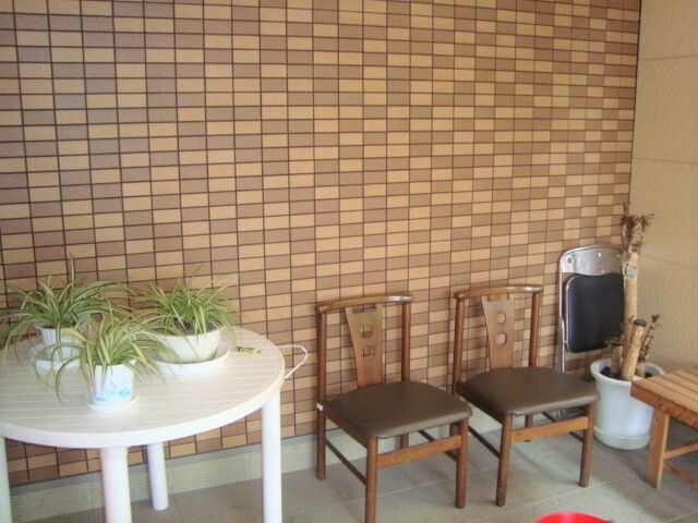 玄関先には観葉植物が置かれた白いテーブルと木製の椅子やベンチ、折り畳み式の椅子などが置かれている。