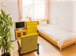 寝具付きのベッドやいす、テレビなどが置かれた一人用の部屋には観葉植物も置かれている。