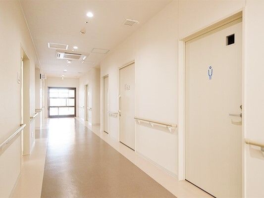 置くまで続いている施設内の廊下の様子。両側に個室のドアと手すりがついている