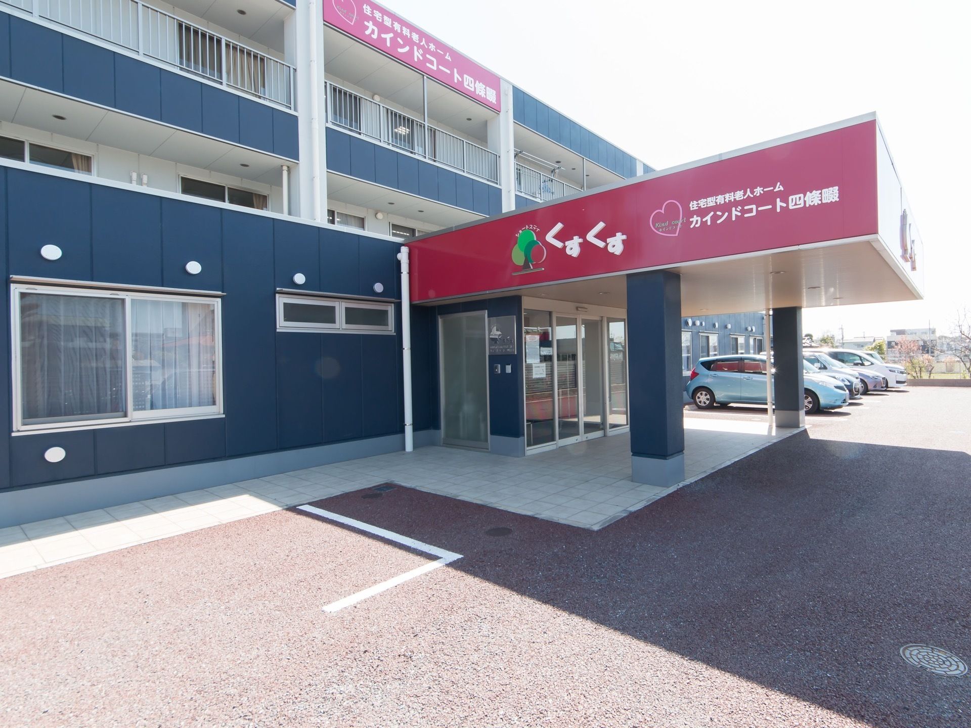 ネイビーとえんじ色を基調としたスタイリッシュなデザインの建物。玄関には、屋根付きの車寄せが設置されている。