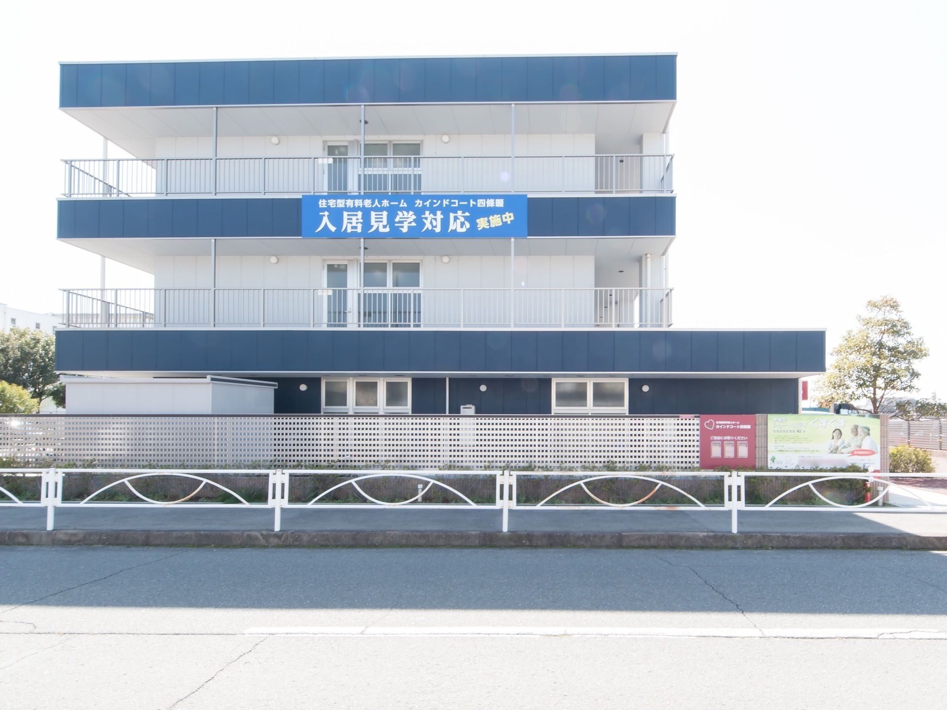 ３階建てのグループホームで、２階以上の部分にはベランダスペースが設けられている。施設目の前は、広い道路が通っている。