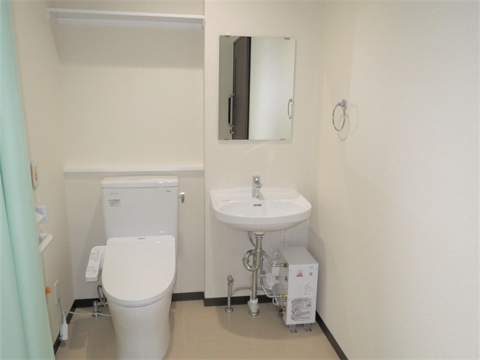 緑のカーテンがドアの代わりに付いたトイレには車いす対応の洗面所があり、洗面所のそばには鏡やタオル掛けがある。