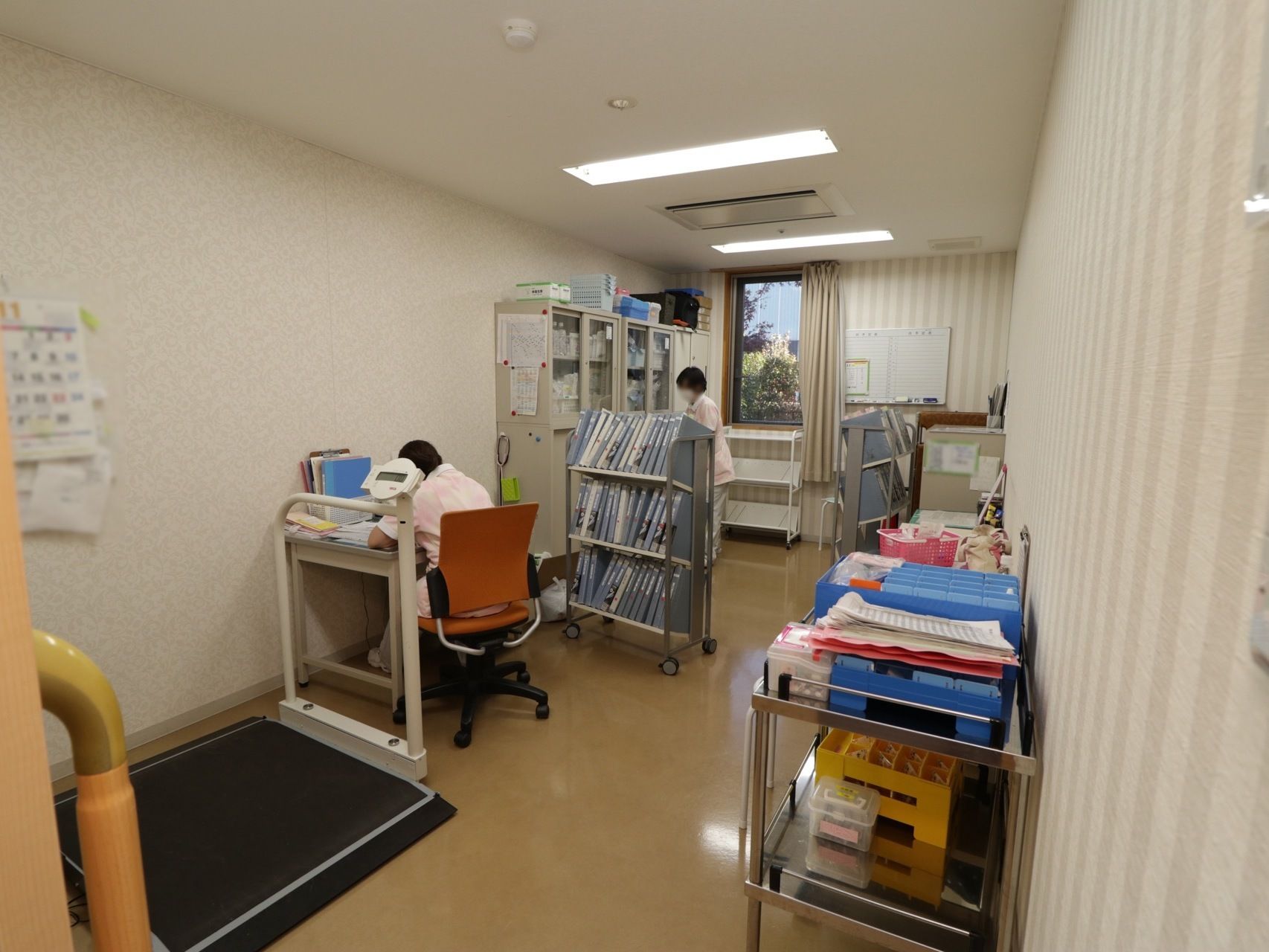 健康管理室には、事務デスクやファイルワゴン、キャビネットが配置されている。車椅子用体重計が置かれている。
