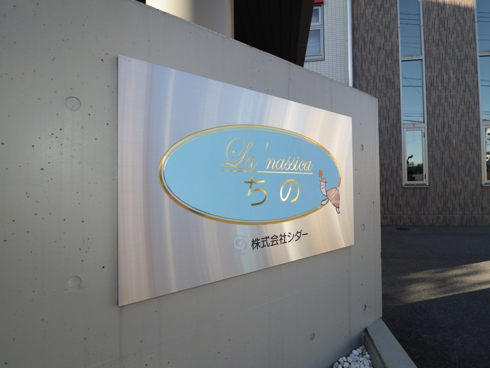 エントランスの原前には、コンクリートの塀が設置されており、施設名が記された金属プレートが取りつけられている。
