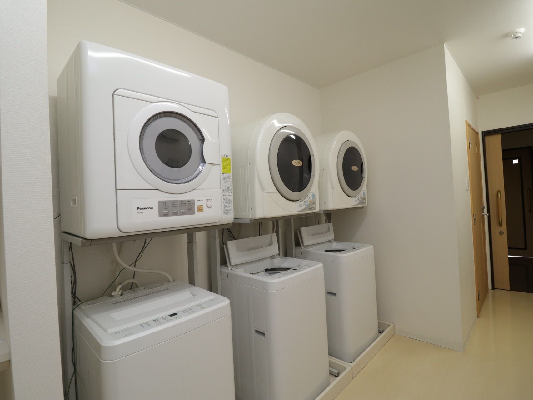 スッキリとした機能的な洗濯室である。壁際に３台の洗濯機と乾燥機が設置されている。出入口の扉には、引き戸が採用されている。