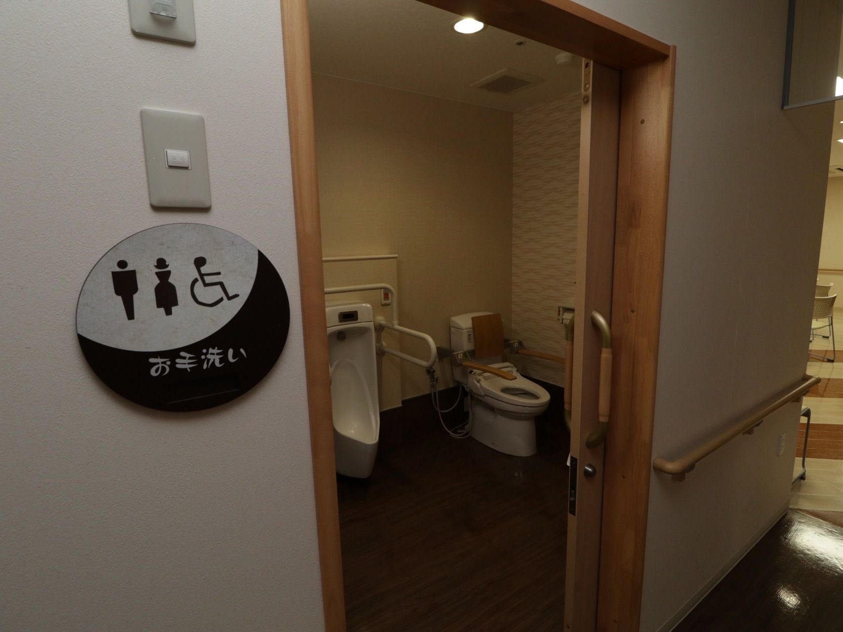 廊下の一角に男女共用トイレが設けられている。男性用小便器と洋式便器が設置されている。扉横の壁には、丸いプレートが掛けられている。