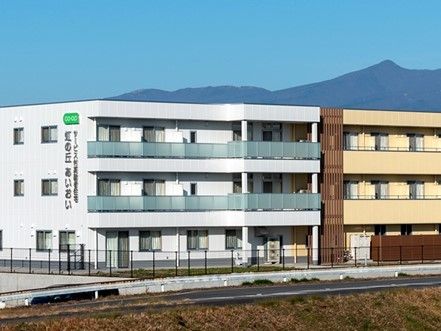 外壁に住宅名が書かれた４階建ての建物。各フロアにベランダが付き、周辺には緑もある。
