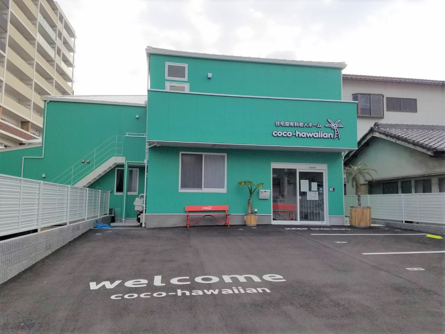 さわやかなグリーンでまとめられた２階建ての建物。玄関脇には赤いベンチがあり、広い駐車場もある。