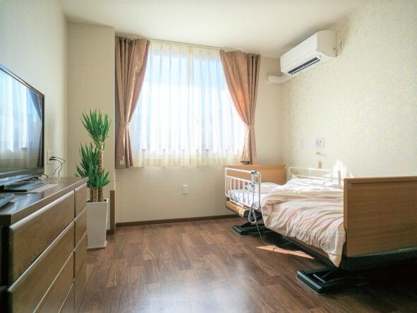 エアコンが付いた居室はフローリングで寝具付きのベッドやテレビなどがあり、観葉植物もある。