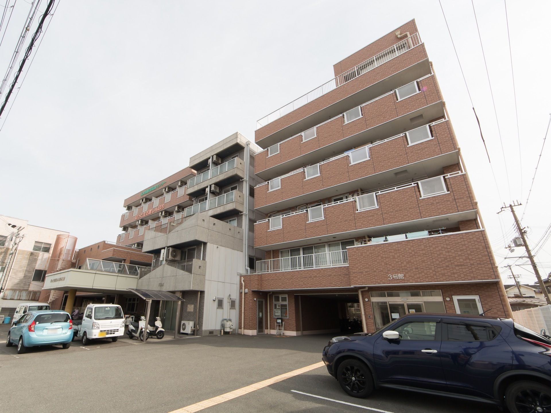 やわらかい色合いの外装の建物が2つ、コンクリート打ちっぱなしの建物を挟んで建てられている。おしゃれなマンションのような外観。